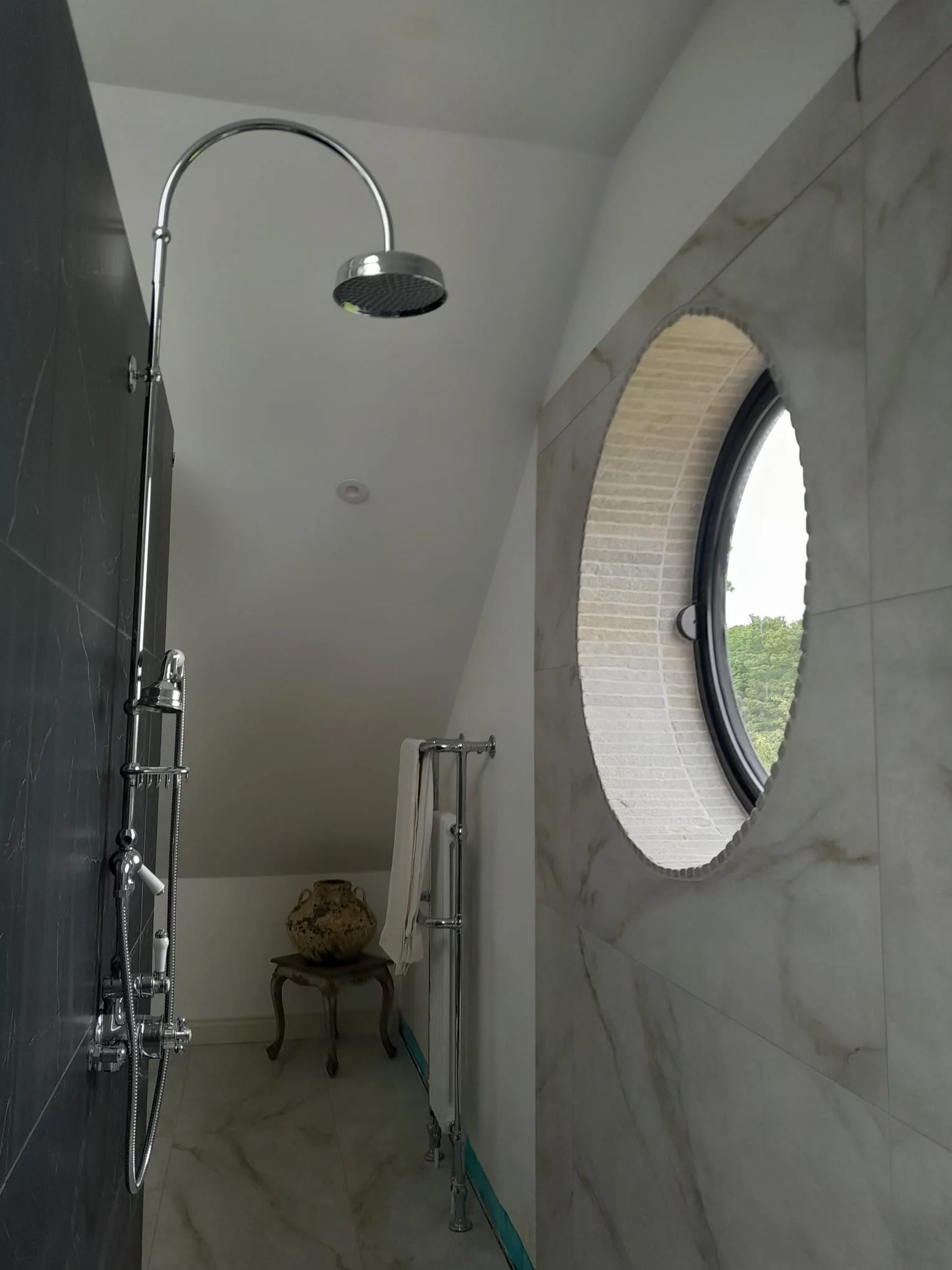 Luxury marble shower room with chrome fittings and porthole window, installed by J1 Plumbing in Harrogate