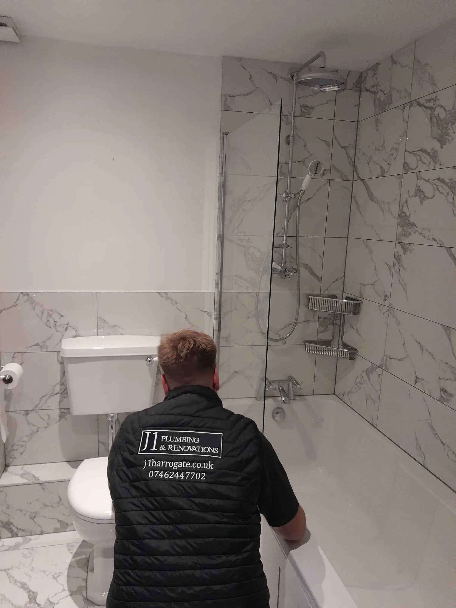 J1 Plumbing tradesman fitting a marble bathroom with walk-in shower and glass screen